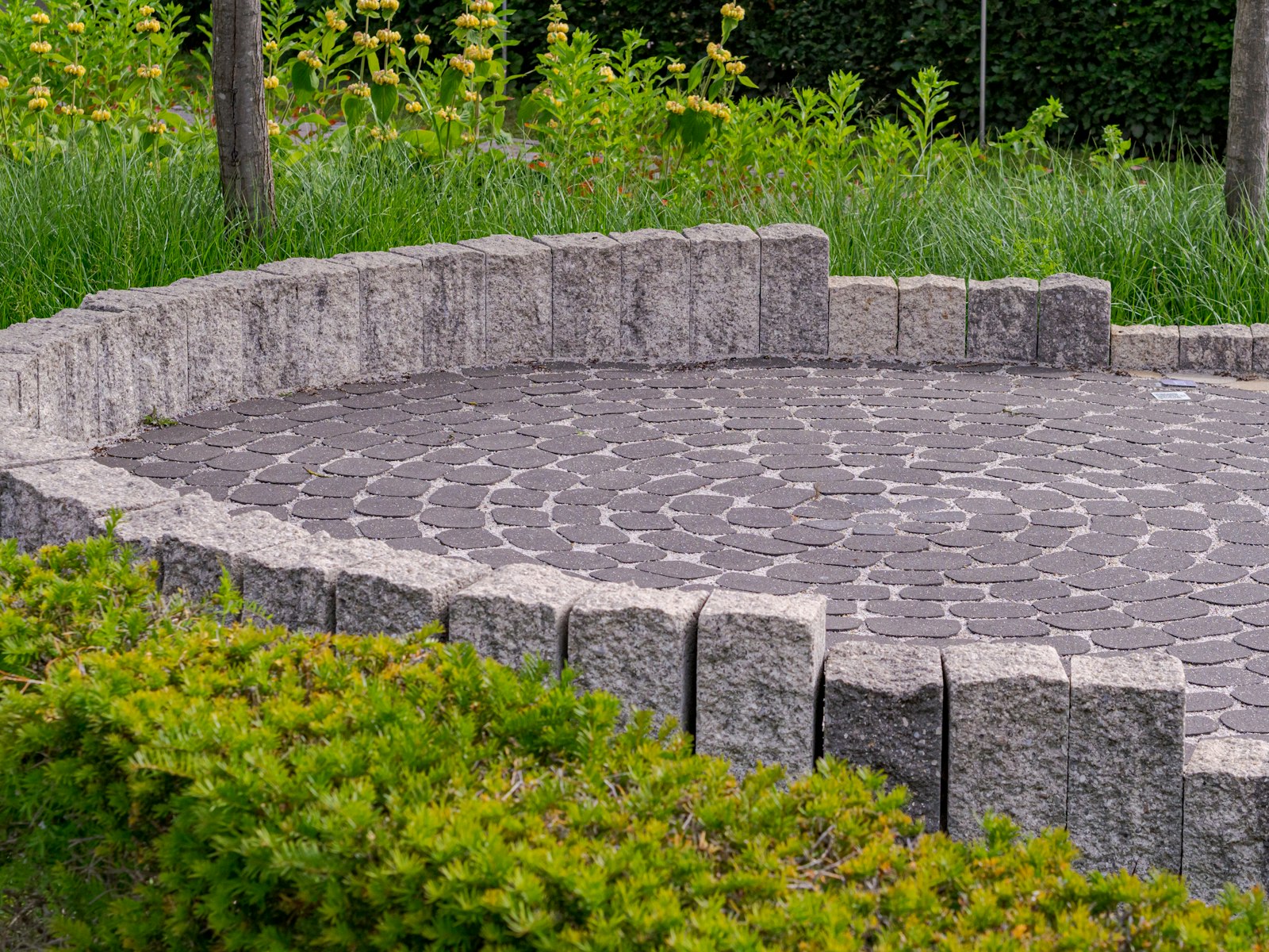 Circular paver patio with a low block seating wall and fresh plantings